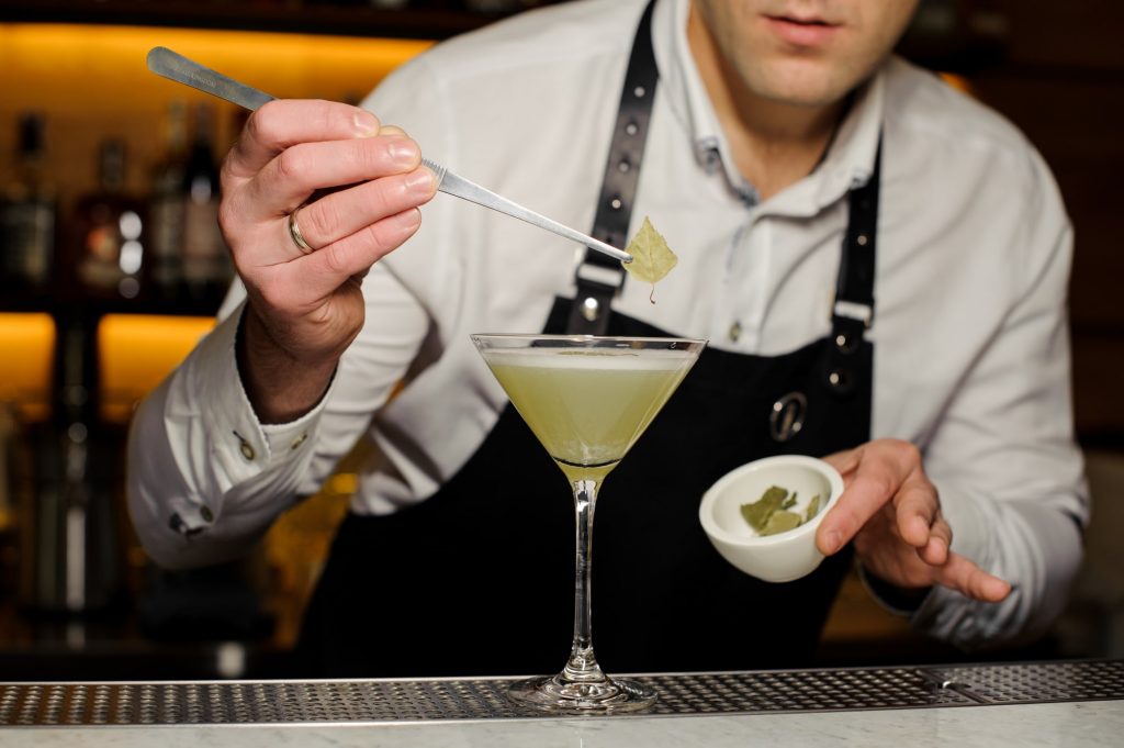 A mixology expert laying a leaf on a cocktail