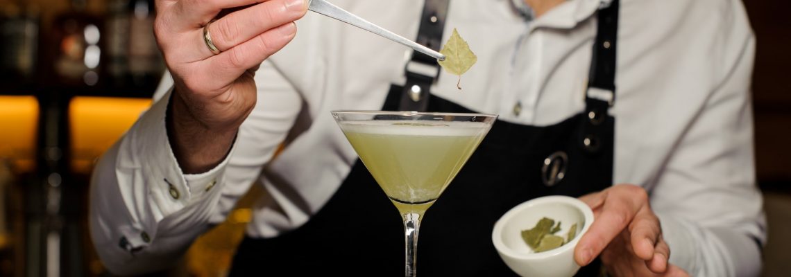 A mixology expert laying a leaf on a cocktail