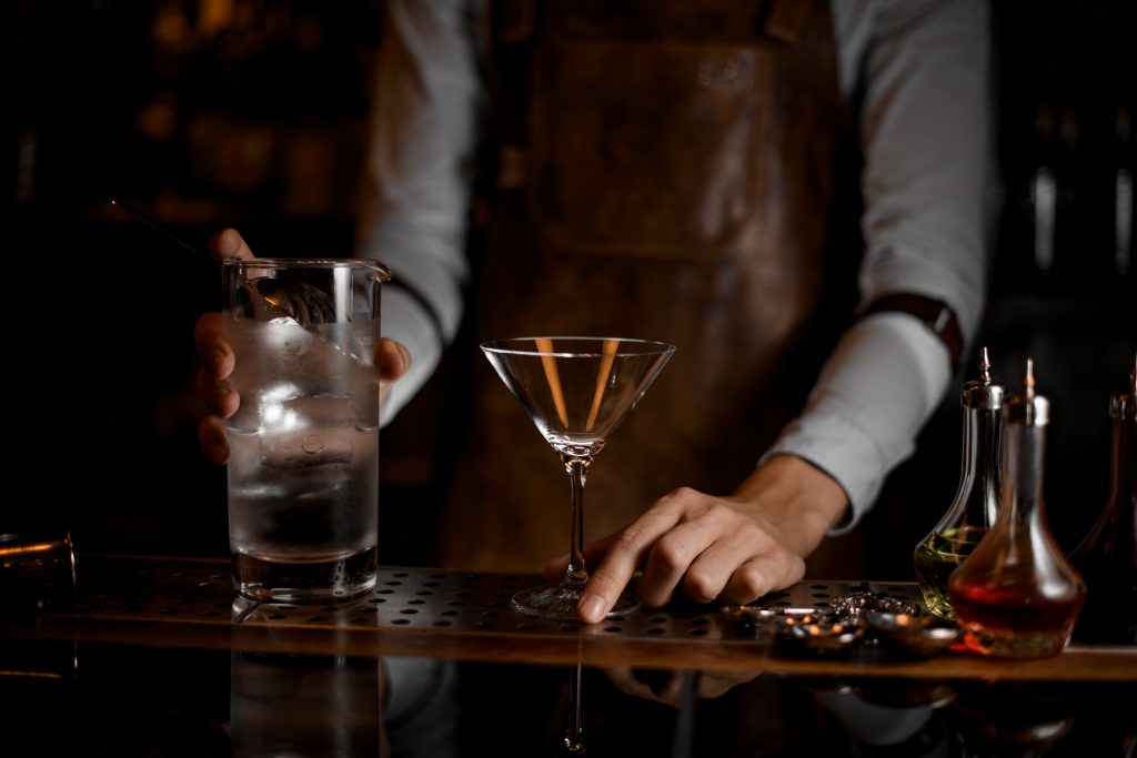 Male bartender prepares to pour a martini cocktail from jar with strainer