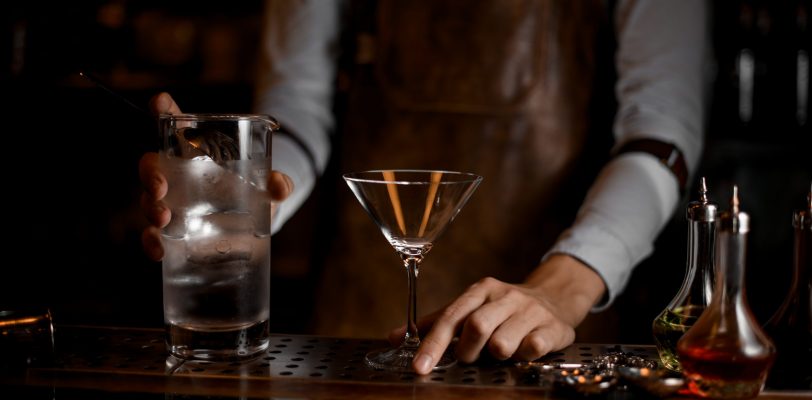 Male bartender prepares to pour a martini cocktail from jar with strainer
